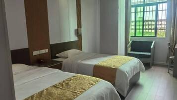 Habitación de hotel con dos camas, una mesita de noche, una silla y una ventana con barrotes.