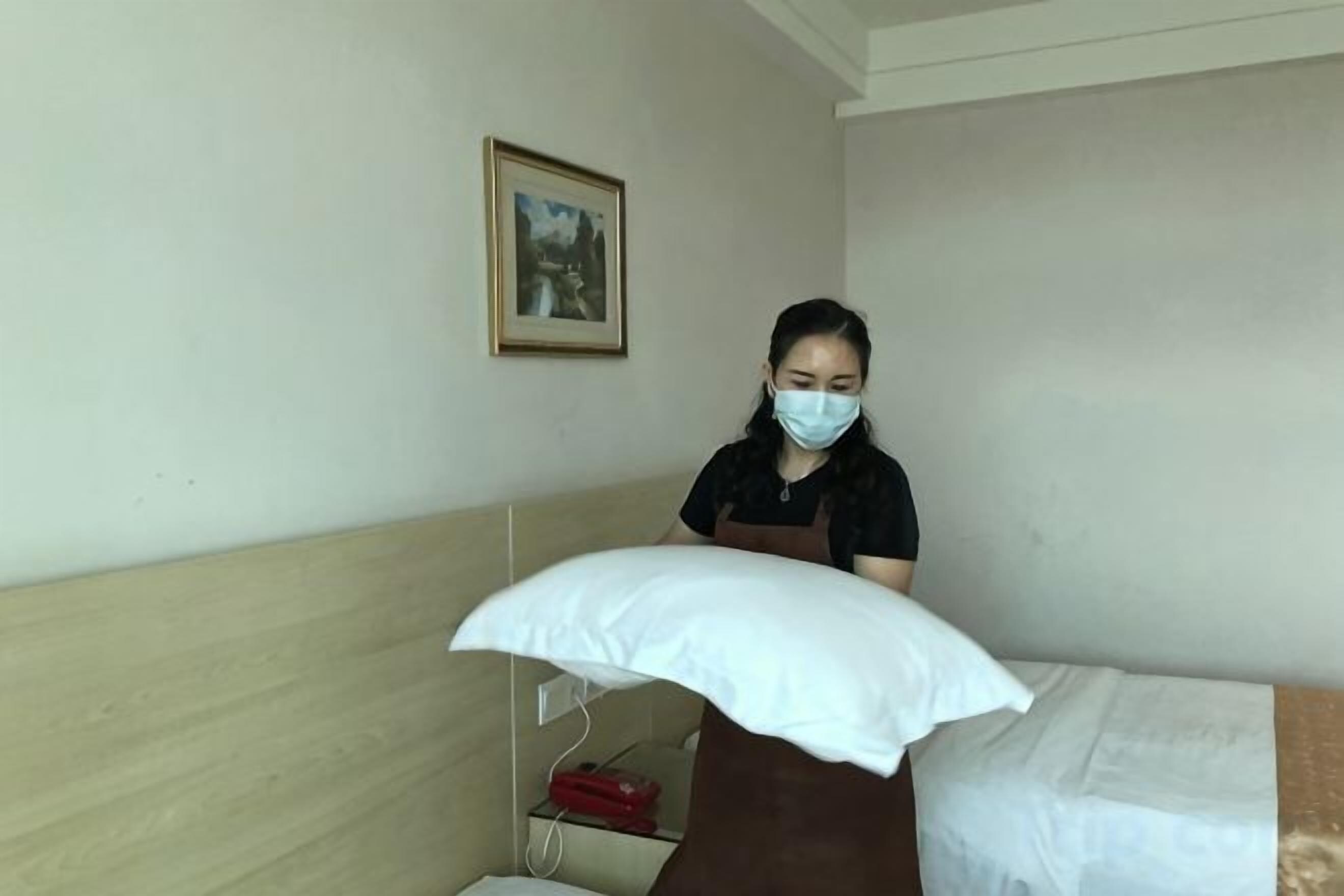 A hotel room with a bed, a pillow, a wall-mounted picture, and a red object on a shelf.