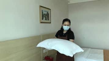 A hotel room with a bed, a pillow, a wall-mounted picture, and a red object on a shelf.