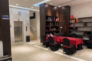 A hotel lobby with a reception desk, a staircase, and a dining area with a red tablecloth. - Nanuo Holiday Hotel (Sanya)