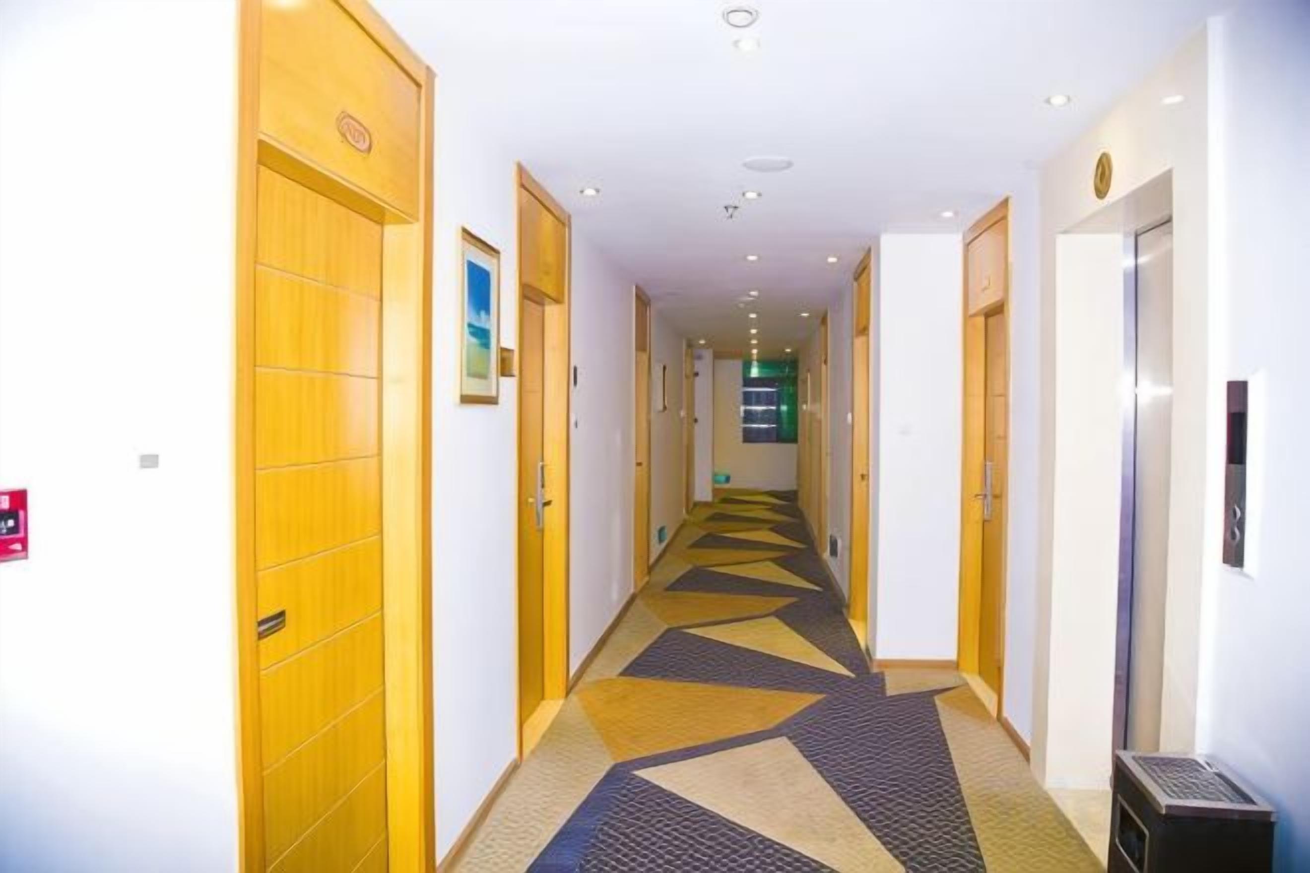 A hotel corridor with wooden doors, a patterned carpet, and a trash bin.