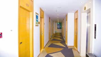 A hotel corridor with wooden doors, a patterned carpet, and a trash bin.