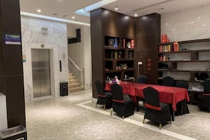 Um hall de hotel com piso de mármore, um balcão de recepção, uma escadaria e um espaço de refeições com mesas e cadeiras.