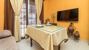 A dining area with a table set for two, a sofa, a TV mounted on the wall, and decorative pottery. - Enjoy Arcos in Arcos de la Frontera (Arcos de la Frontera)