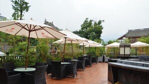 An outdoor seating area with wicker tables and chairs, covered by large umbrellas, and a bar counter. - Starway Hotel (Dujiangyan Scenic Area Nanqiao) (Dujiangyan)