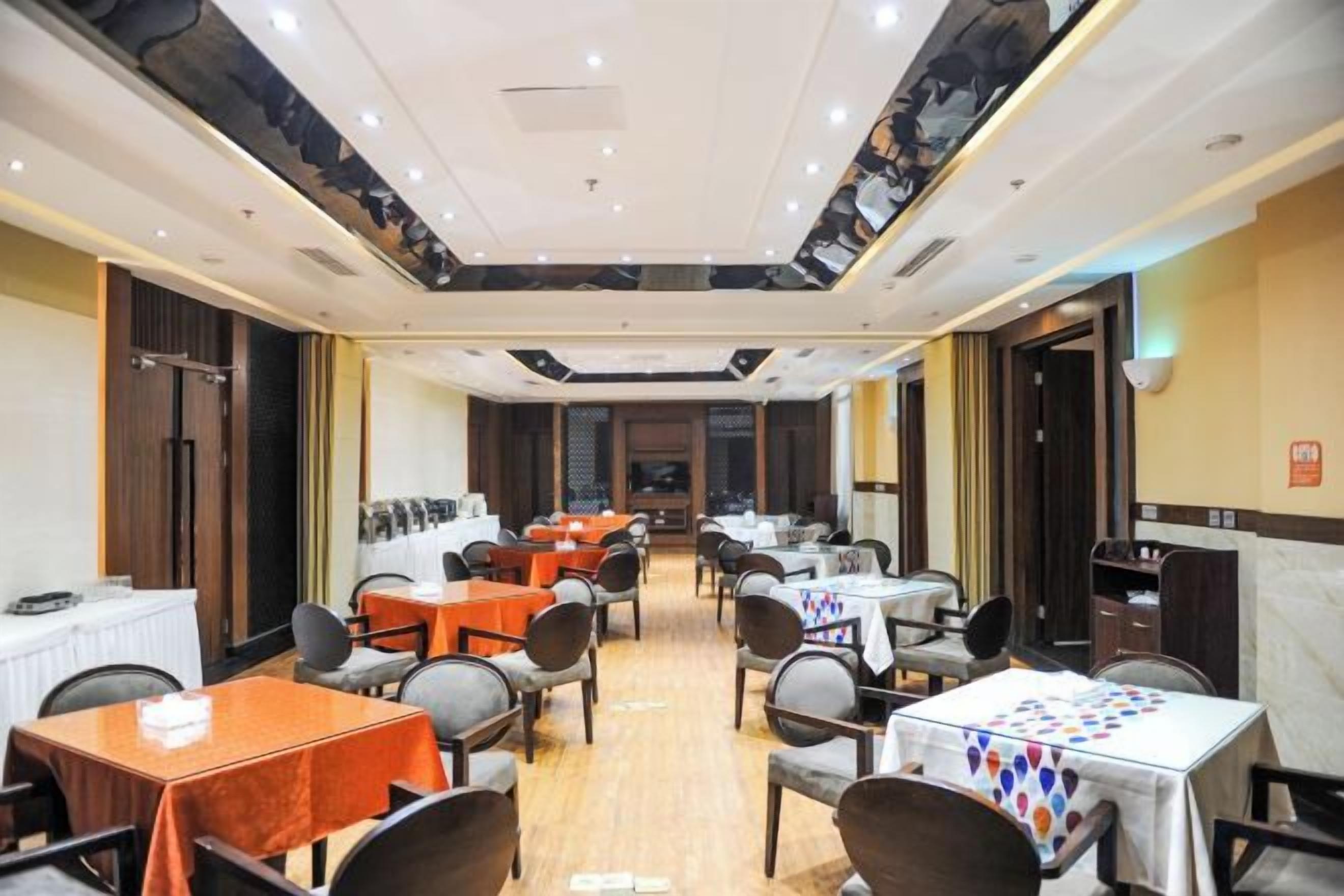 A hotel dining area with multiple tables and chairs, a chandelier, and a view of the cityscape through the windows.