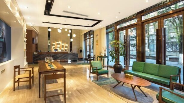 A spacious lobby with a wooden reception desk, a green sofa, and a dining area with a wooden table and chairs. - Starway Hotel (Dujiangyan Scenic Area Nanqiao) (Dujiangyan)