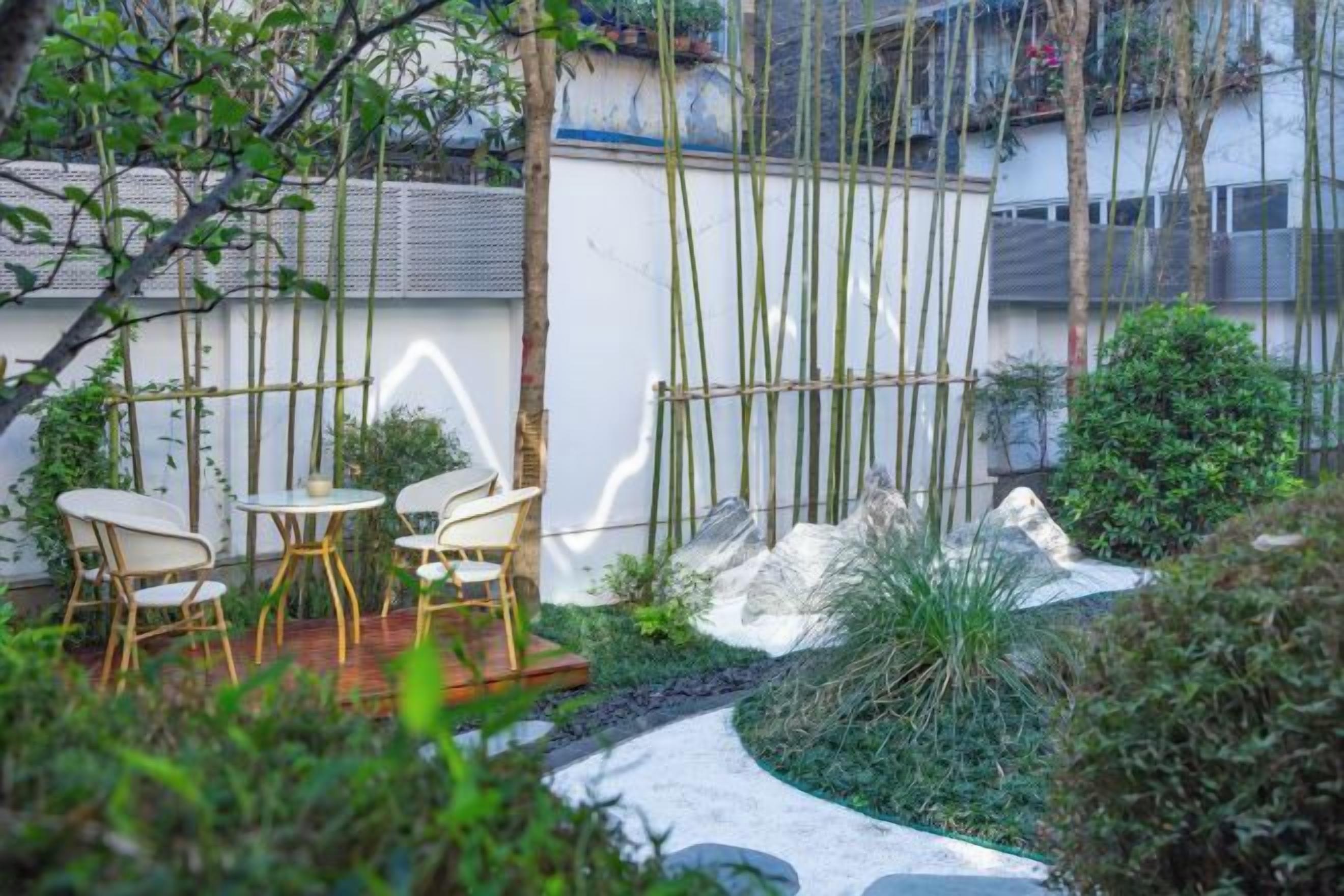 A garden with a wooden deck, chairs, and a white wall.