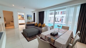 A modern hotel room with a living area, dining table, and a view of a swimming pool. - B14 - 2 Bedroom Serviced Apt with Pool Access, Karon Beach (Tambon Karon)
