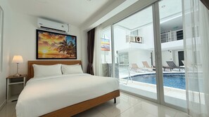 Una camera d'hotel con un letto, un quadro, un condizionatore d'aria, una finestra vista piscina e lettini, e un cartello di uscita.