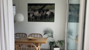 En matplats med ett träbord och stolar, en hängande lampa, en tavla med får som hänger på väggen och krukväxter.
