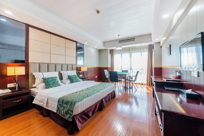 A hotel room with a large bed, a desk, a chair, a TV, and a window.