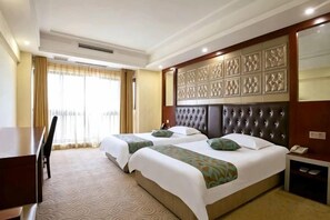 Habitación de hotel con dos camas, un escritorio, una silla y un ventanal con cortinas.