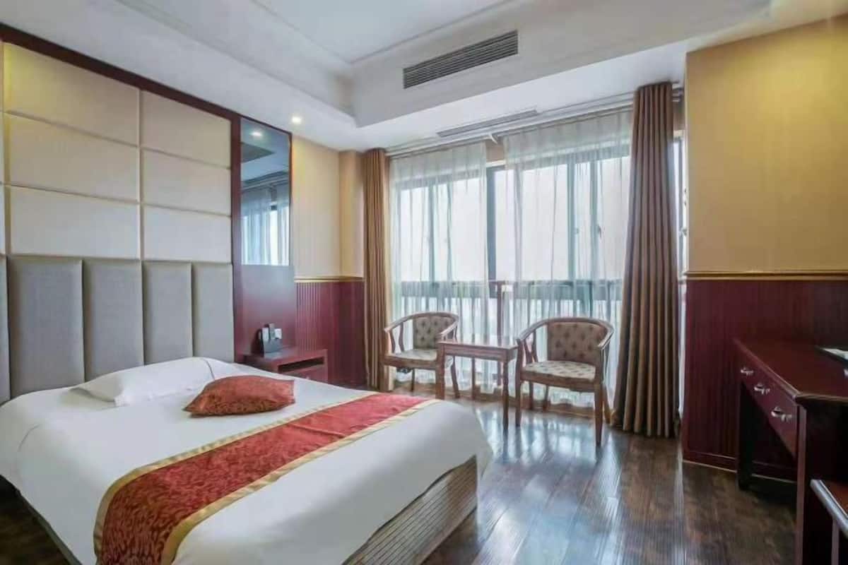 Une chambre d’hôtel avec un grand lit, un bureau, deux chaises et un balcon avec des rideaux.