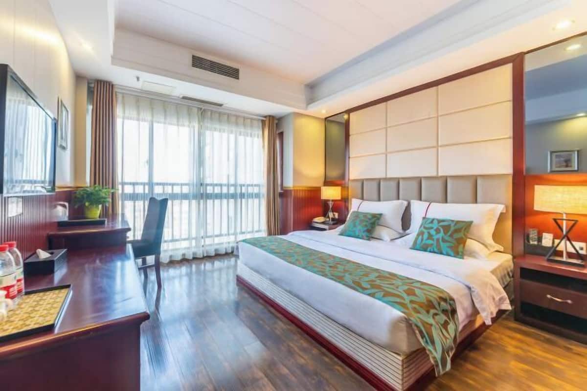 Une chambre d’hôtel avec un grand lit, un bureau, une chaise et une fenêtre avec des rideaux.
