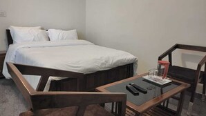 A bedroom with a bed, two wooden chairs, a small table with a glass, and a remote control. - Durai Residency (Kodaikanal)