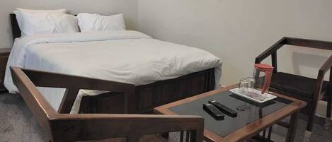 A bedroom with a bed, two wooden chairs, a small table with a glass, and a remote control.