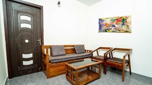 A room with a dark wooden door, a wooden sofa with cushions, a glass coffee table, and two wooden chairs. - Durai Residency (Kodaikanal)