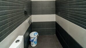 A narrow bathroom with black and white striped walls, a toilet, a bidet, and a bucket with a blue handle. - Durai Residency (Kodaikanal)