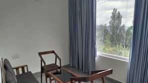 A room with a sofa, two wooden chairs, a glass-top table, and a view of trees through large windows. - Durai Residency (Kodaikanal)