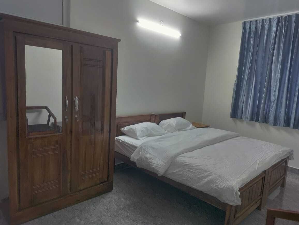 A bedroom with a wooden wardrobe, a bed with white bedding, and a window with blue curtains.