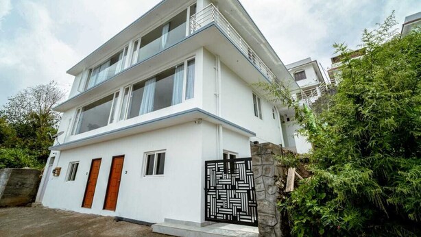A modern two-story building with a white facade, multiple windows, and a black decorative gate. - Durai Residency (Kodaikanal)