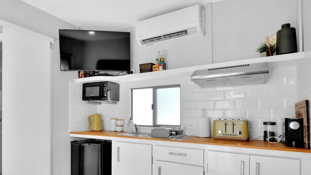 Een moderne keuken met witte kasten, een zwarte koelkast, een magnetron, een broodrooster en een televisie.