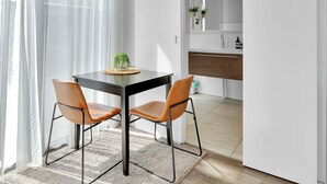 Een moderne eetruimte met een tafel en twee stoelen, een keuken met een houten aanrecht en spoelbak, en uitzicht door een open deur.