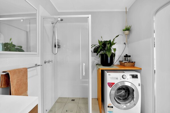 A modern bathroom with a shower, a washing machine, a mirror, and a potted plant.