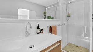 Een moderne badkamer met een wit wastafelmeubel, een douchecabine van glas en een grote spiegel.