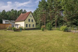 Ein zweistöckiges Haus mit rotem Ziegeldach, umgeben von einem gepflegten Rasen und dichtem Wald.