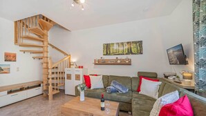 A modern living room with a wooden staircase, a sofa set, a coffee table, and a flat-screen TV. - Cozy vacation apartment in the countryside, with sauna and garden (Garz)