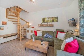 A modern living room with a wooden staircase, a sofa set, a coffee table, and a flat-screen TV. - Cozy vacation apartment in the countryside, with sauna and garden (Garz)