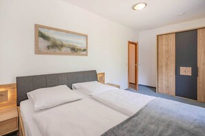 A bedroom with a bed, a nightstand, a bedside table, a wooden door, and a painting on the wall. - Cozy vacation apartment in the countryside, with sauna and garden (Garz)