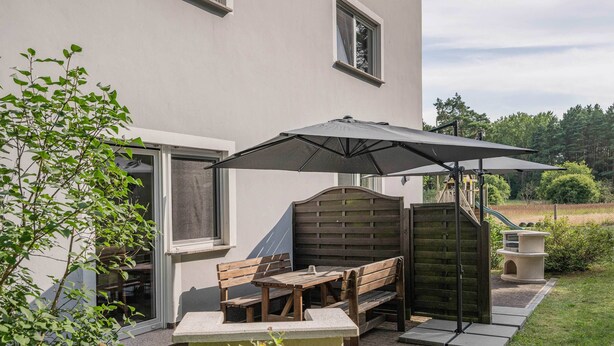 A patio with a table and chairs, an umbrella, and a wooden fence. - Cozy vacation apartment in the countryside, with sauna and garden (Garz)