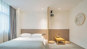 Une chambre d’hôtel moderne avec un grand lit, une tête de lit en bois, une petite table en bois et un projecteur fixé au mur.
