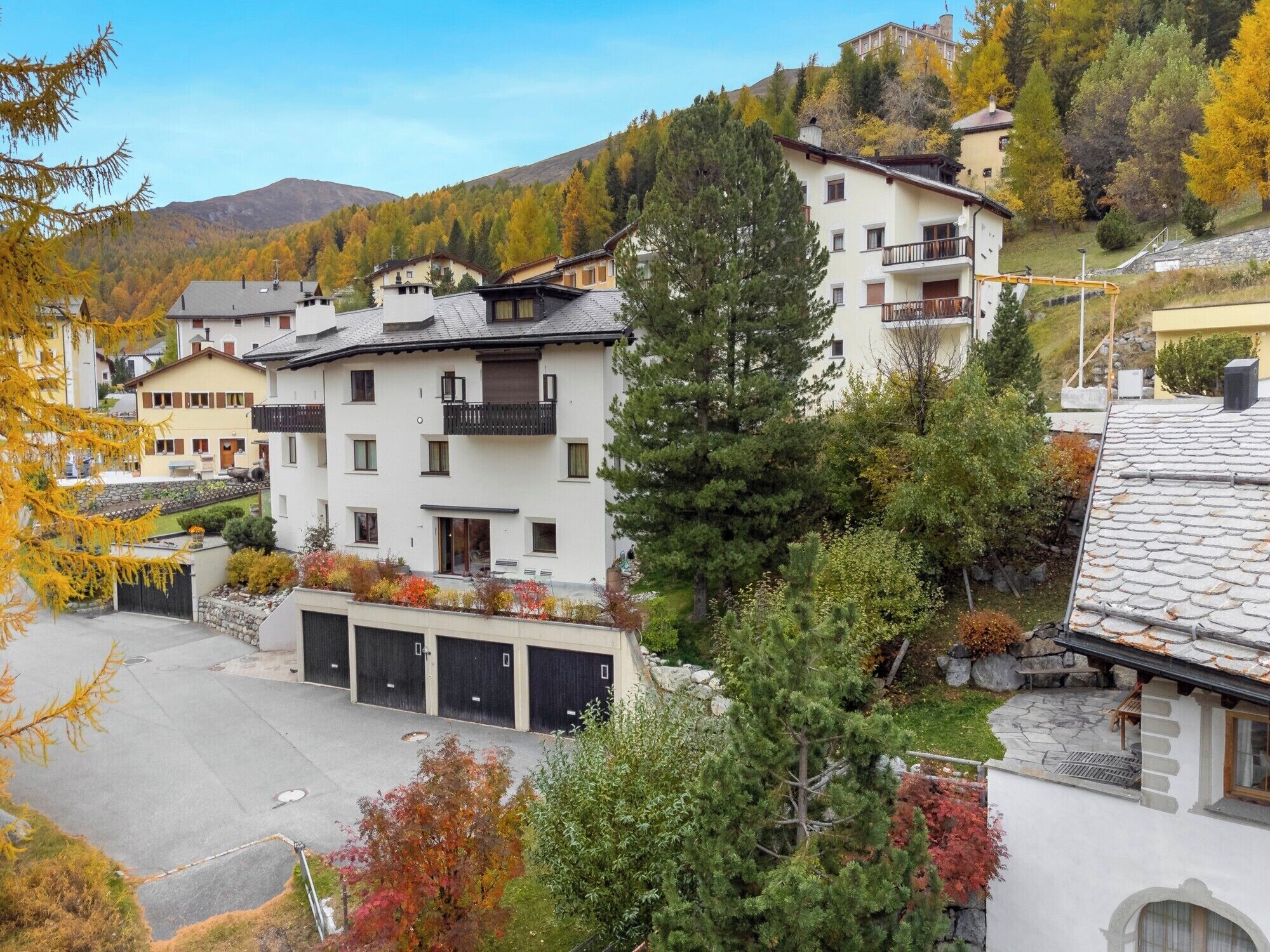 A multi-story building with a balcony, surrounded by autumn foliage and a mountainous backdrop.