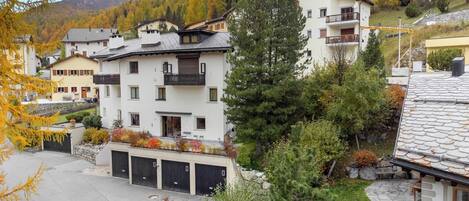 A multi-story building with a balcony, surrounded by autumn foliage and a mountainous backdrop.