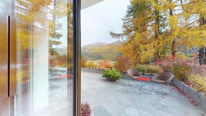 Une terrasse avec un sol en pierre, du mobilier d’extérieur et une vue sur les arbres et les montagnes aux couleurs automnales.
