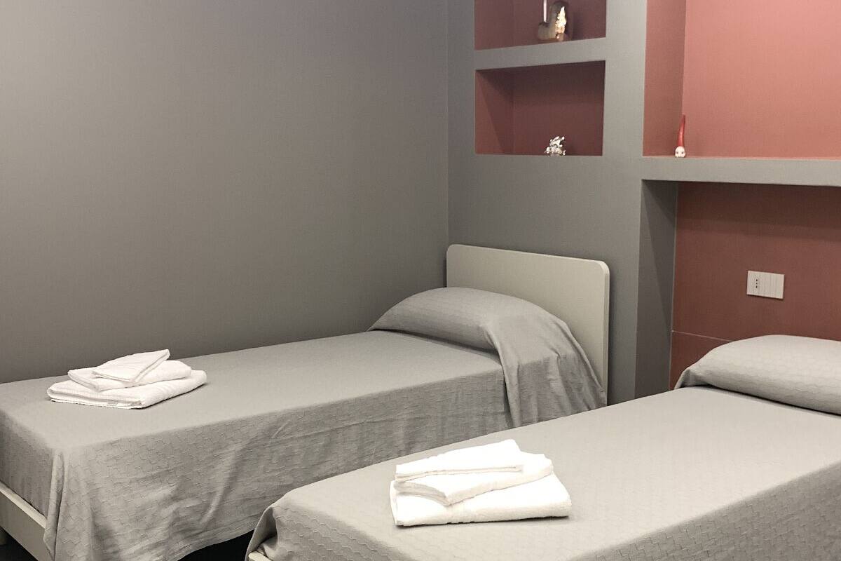 A room with two single beds, grey bedding, and a red accent wall.