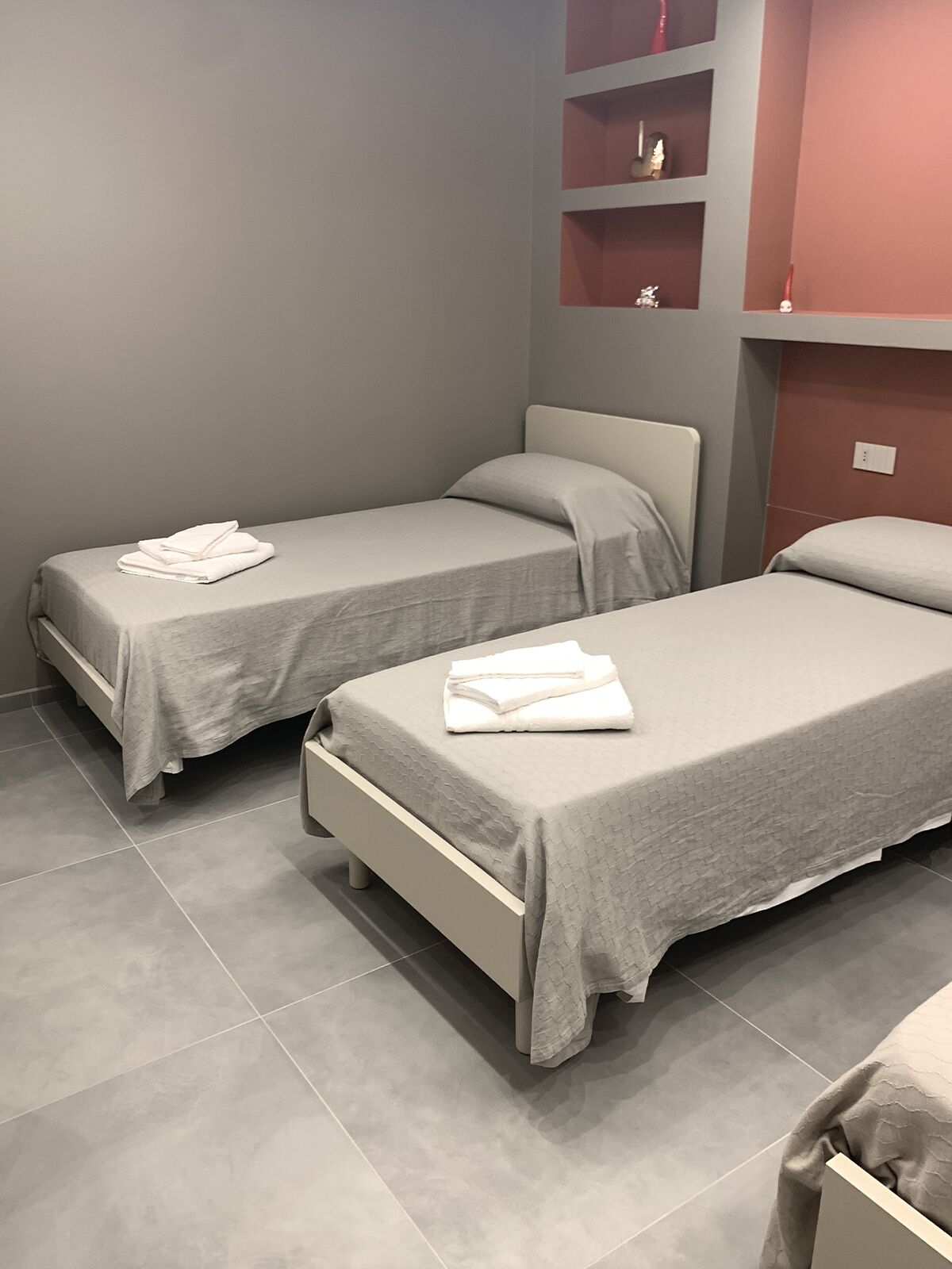 A hotel room with two single beds, grey bedding, and a tiled floor.