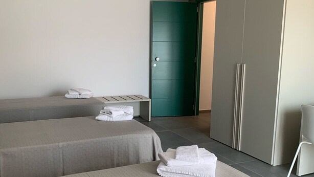 Moderni hotellihuone, jossa on kaksi sänkyä, vaatekaappi ja vihreät ovet.