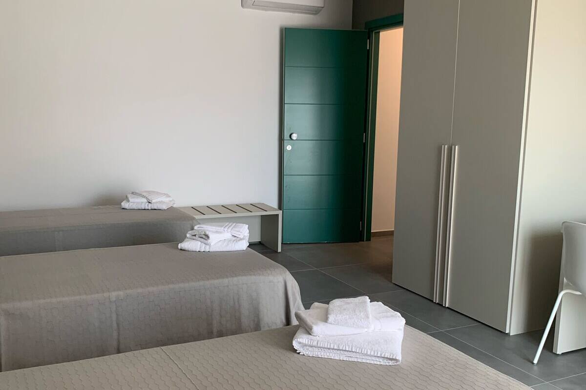 A modern hotel room with two beds, a wardrobe, and a green door.