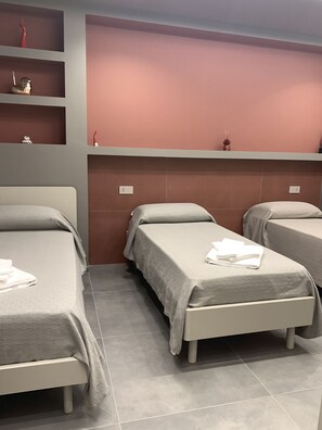 A hotel room with three single beds, a built-in shelf with decorative items, and a plain wall. - B&B The Princess (Montecorvino Pugliano)