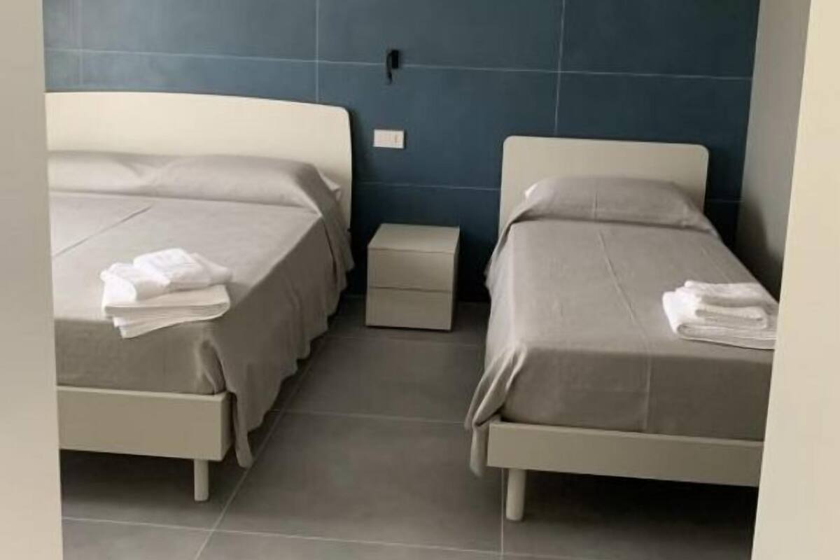 A hotel room with two single beds, a small bedside table, and a nightstand.