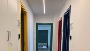 Käytävällä on ovia, jotka johtavat huoneisiin, taustalla näkyy sänky ja katossa on moderni valaisin.