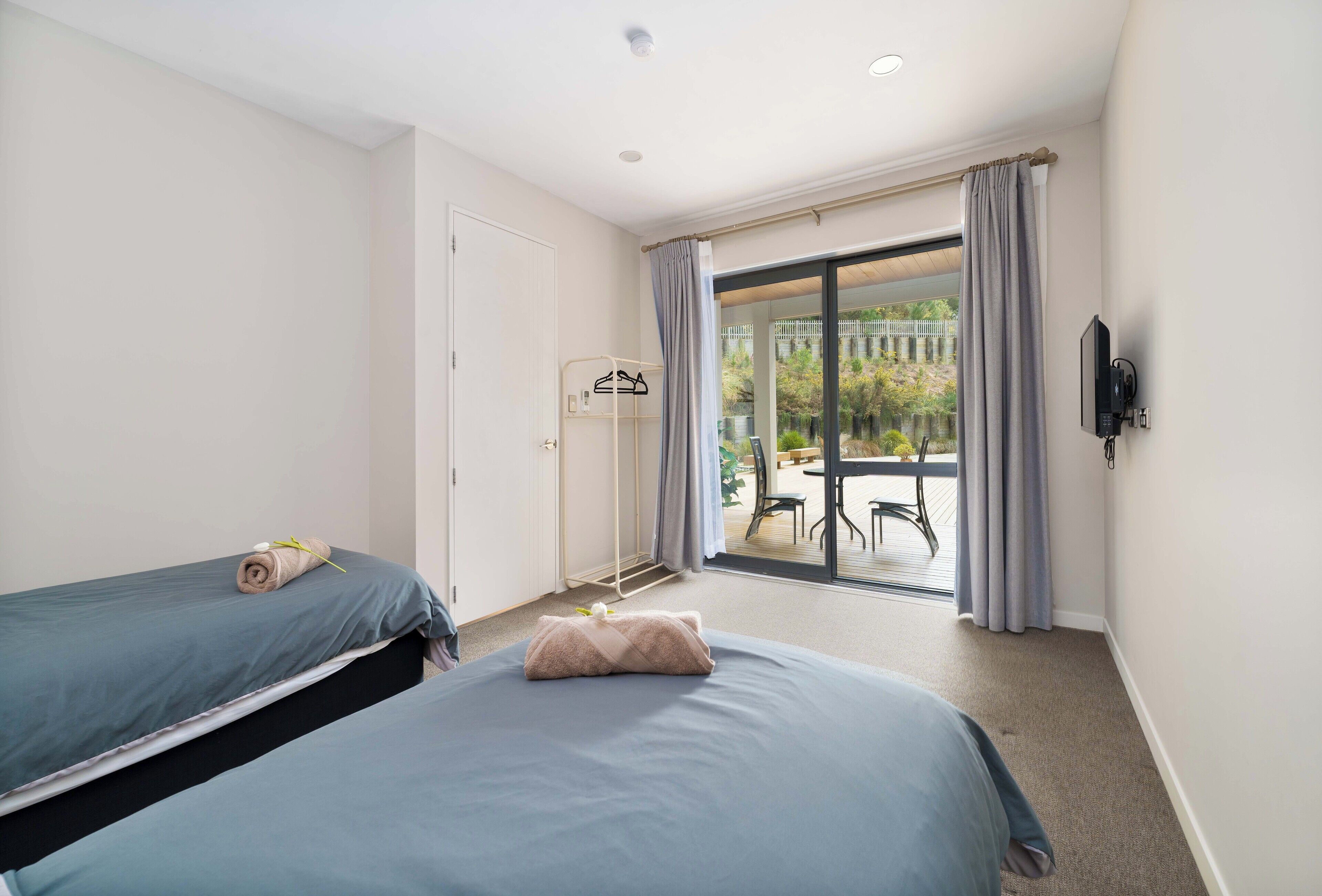 A hotel room with two beds, a balcony with a table and chairs, and a TV mounted on the wall.