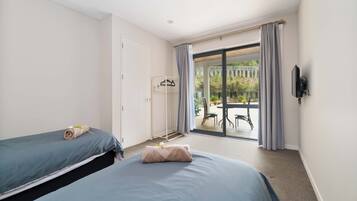 A hotel room with two beds, a balcony with a table and chairs, and a TV mounted on the wall.