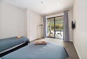 A hotel room with two beds, a balcony with a table and chairs, and a TV mounted on the wall.