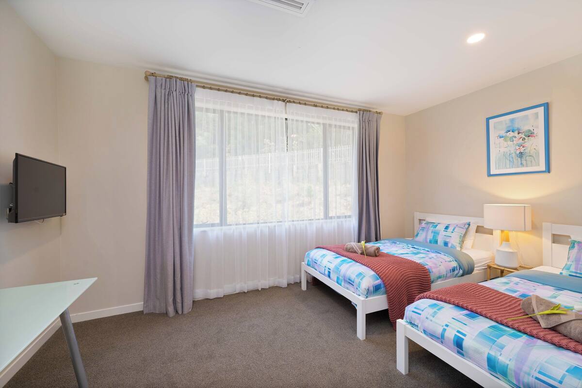 A bedroom with two beds, a TV, and a window with curtains.